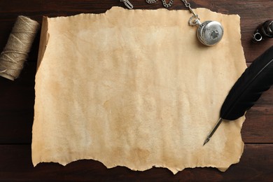 Sheet of old parchment paper, black feather, inkwell, rope and pocket chain clock on wooden table, flat lay