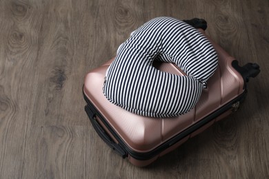 Photo of Striped travel pillow and suitcase on floor, space for text