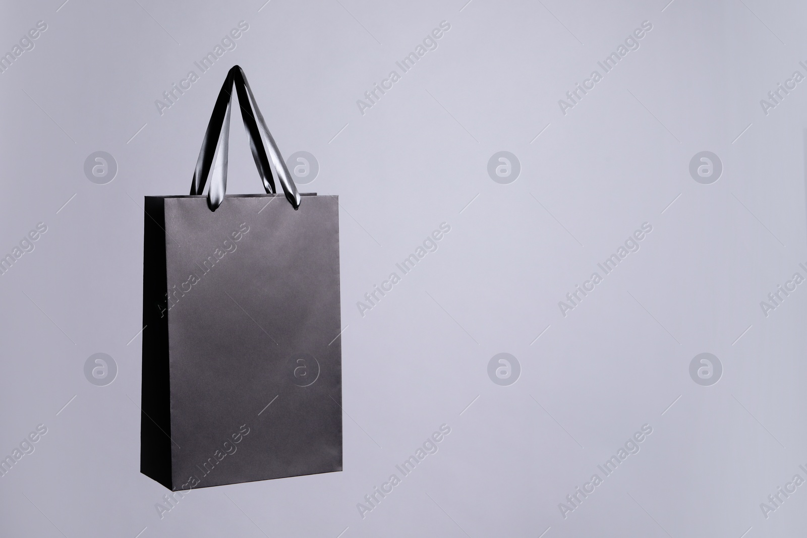 Photo of One black paper shopping bag on grey background. Space for text