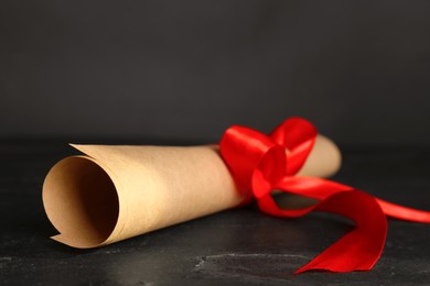Photo of Rolled student's diploma with red ribbon on black table, closeup