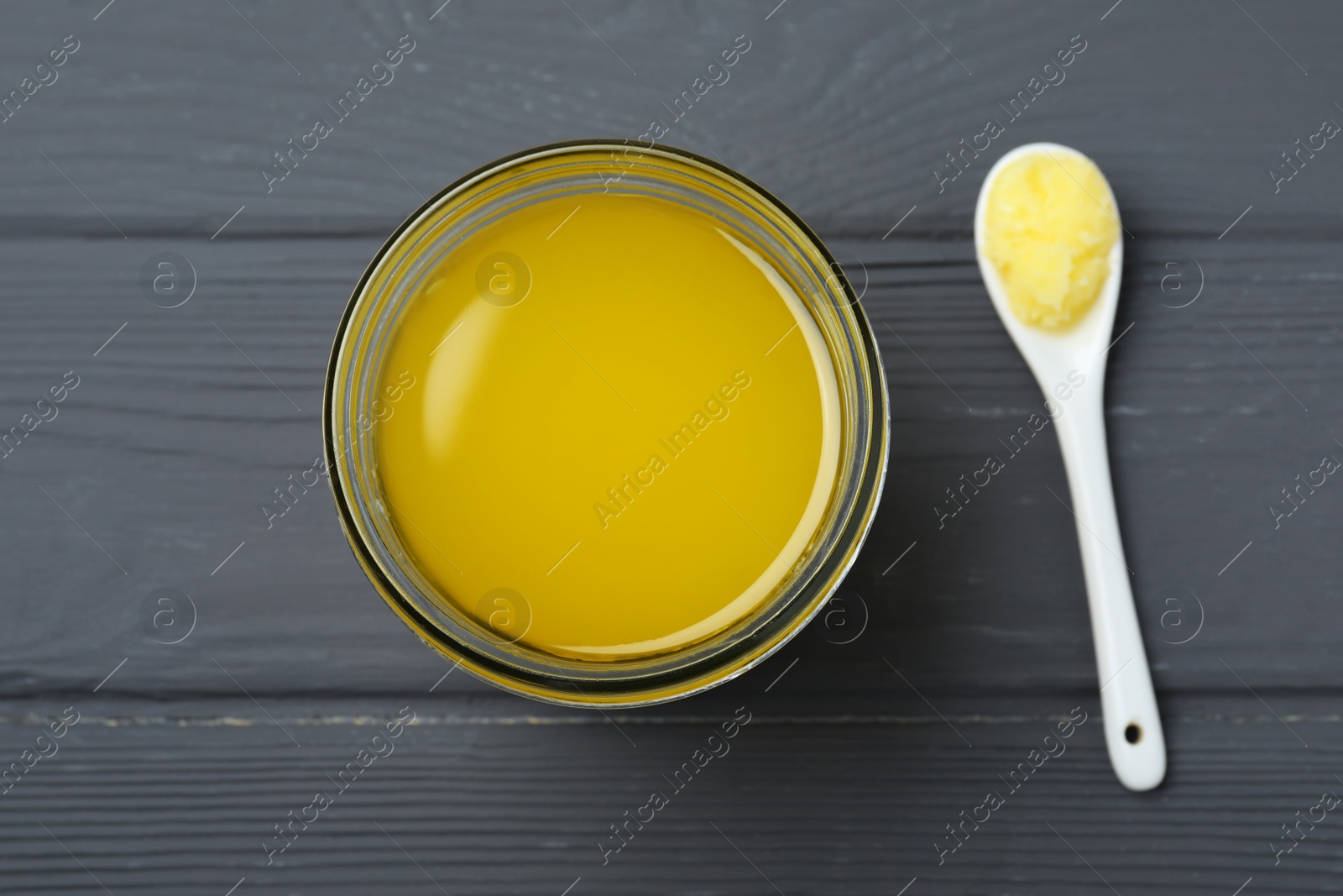 Photo of Glass jar and spoon of Ghee butter on grey wooden table, flat lay