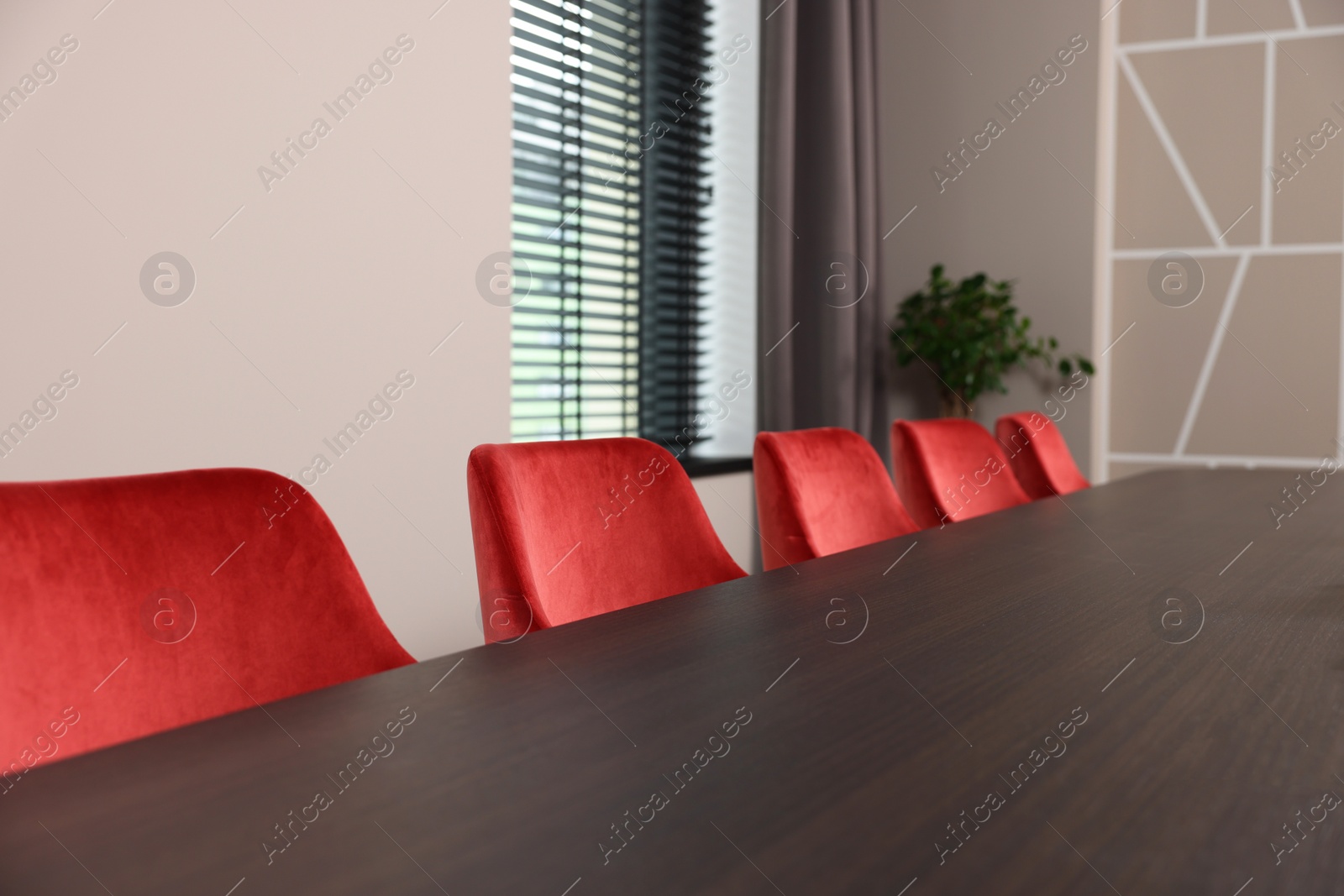 Photo of Stylish red office chairs and large wooden table in empty conference room