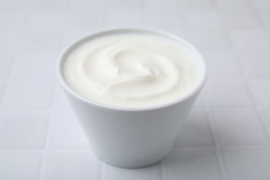 Delicious natural yogurt in bowl on white tiled table, closeup