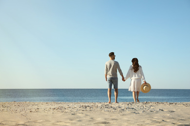 Photo of Young couple walking on beach near sea, back view. Honeymoon trip