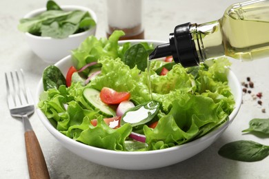 Photo of Pouring oil into salad on light grey table, closeup