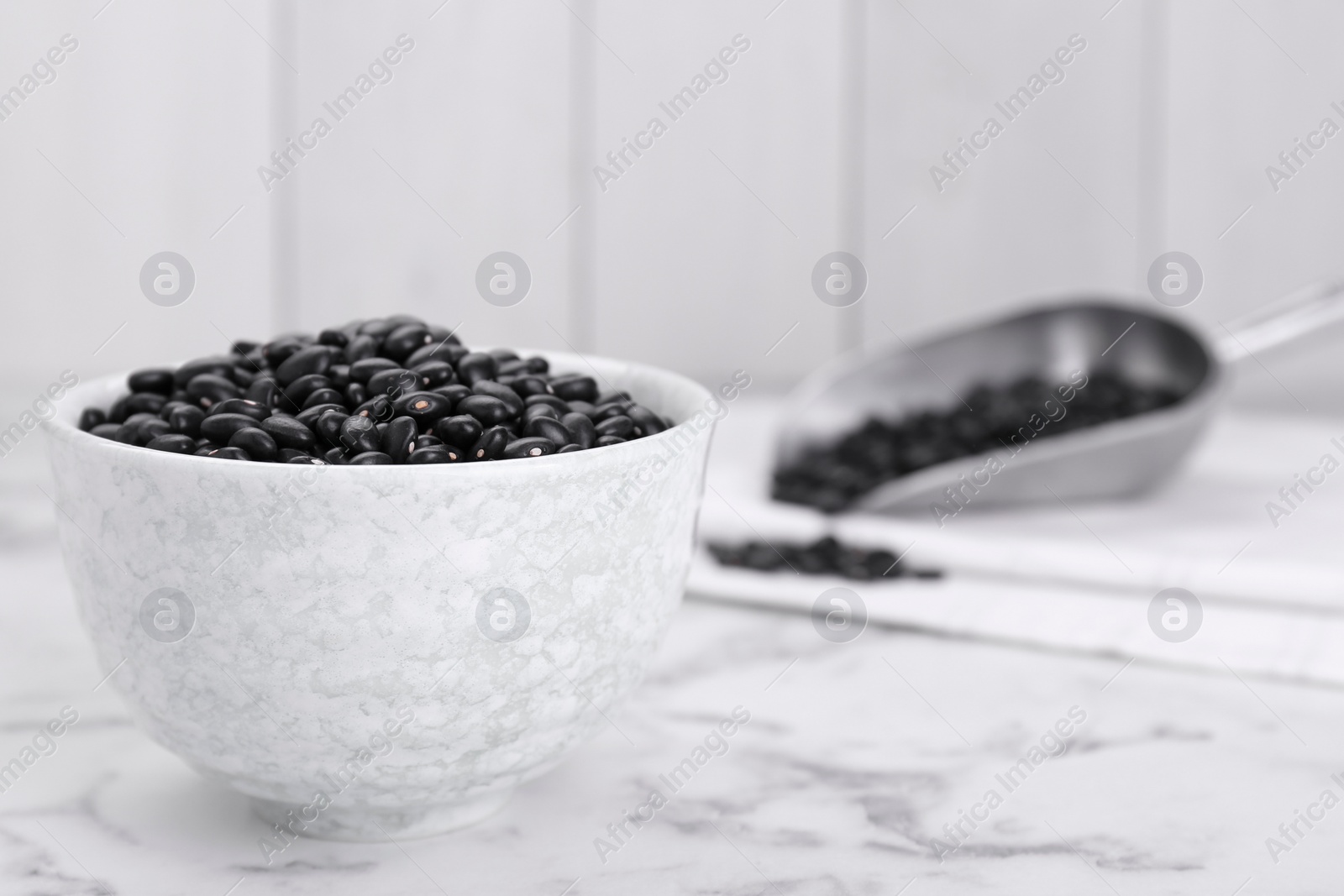 Photo of Bowl of raw black beans on white marble table. Space for text