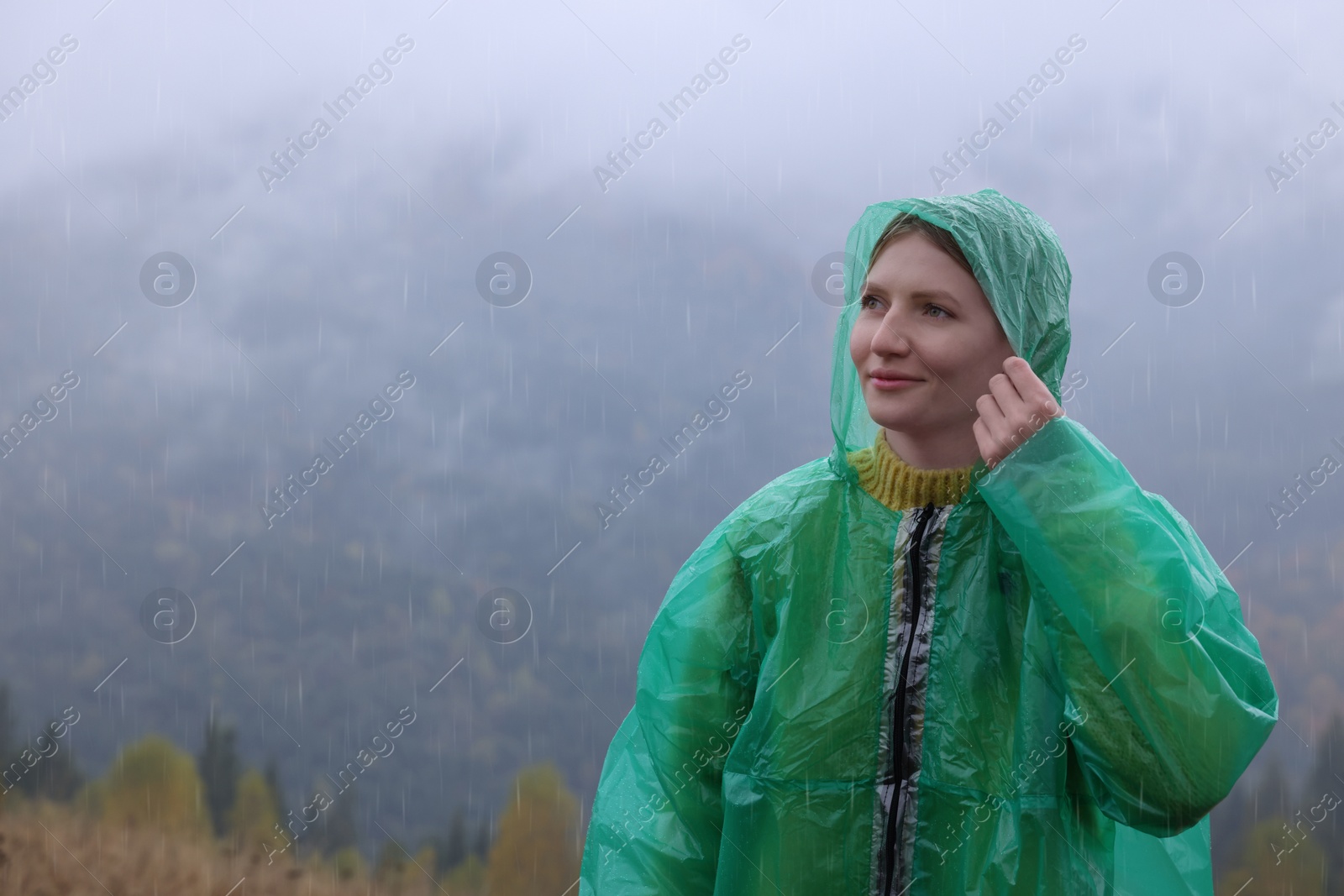 Photo of Young woman in raincoat enjoying mountain landscape under rain