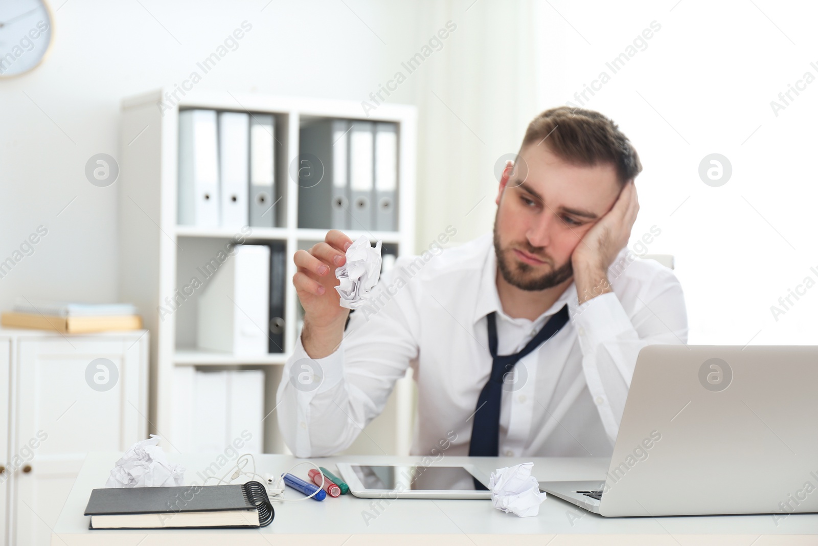 Photo of Lazy young man with crumpled paper at messy table in office, focus on hand