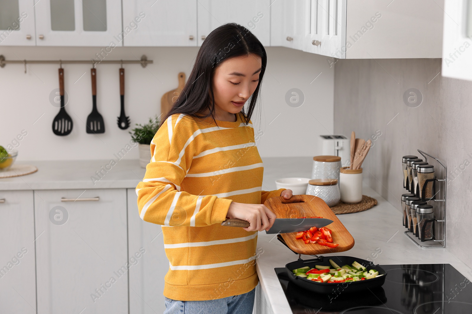 Photo of Cooking process. Beautiful woman adding cut bell pepper into pan with vegetables in kitchen. Space for text