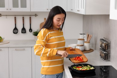 Cooking process. Beautiful woman adding cut bell pepper into pan with vegetables in kitchen. Space for text