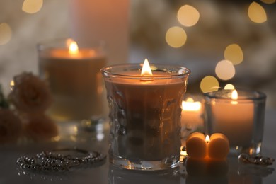 Burning candles, flowers and jewelry on table, closeup view