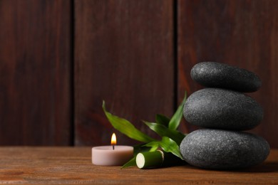 Spa stones, burning candle and bamboo sprout on wooden table. Space for text