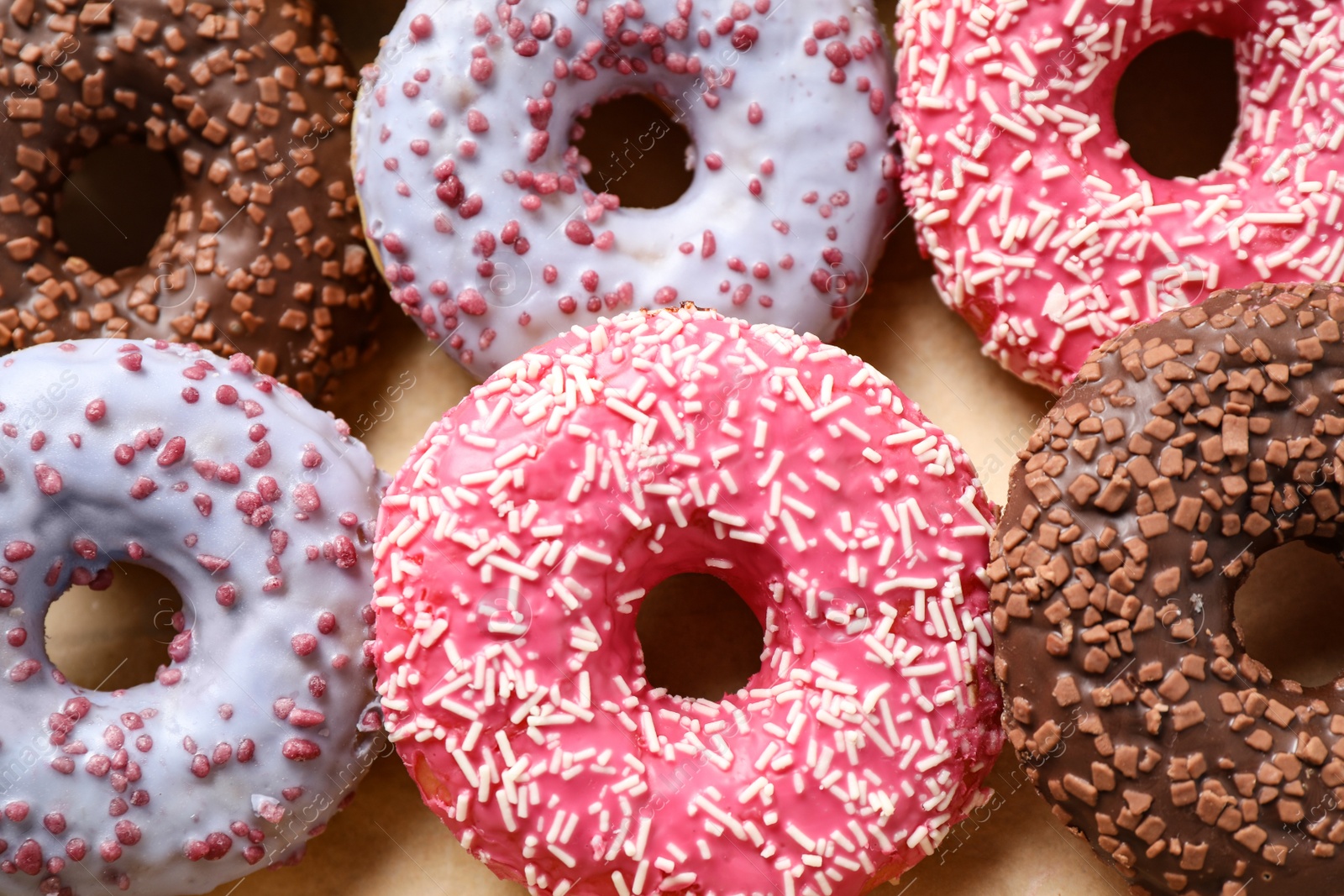 Photo of Delicious glazed donuts on parchment paper, closeup. Sweet pastries