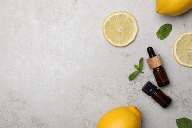 Photo of Bottles of citrus essential oil and fresh lemons on light table, flat lay. Space for text