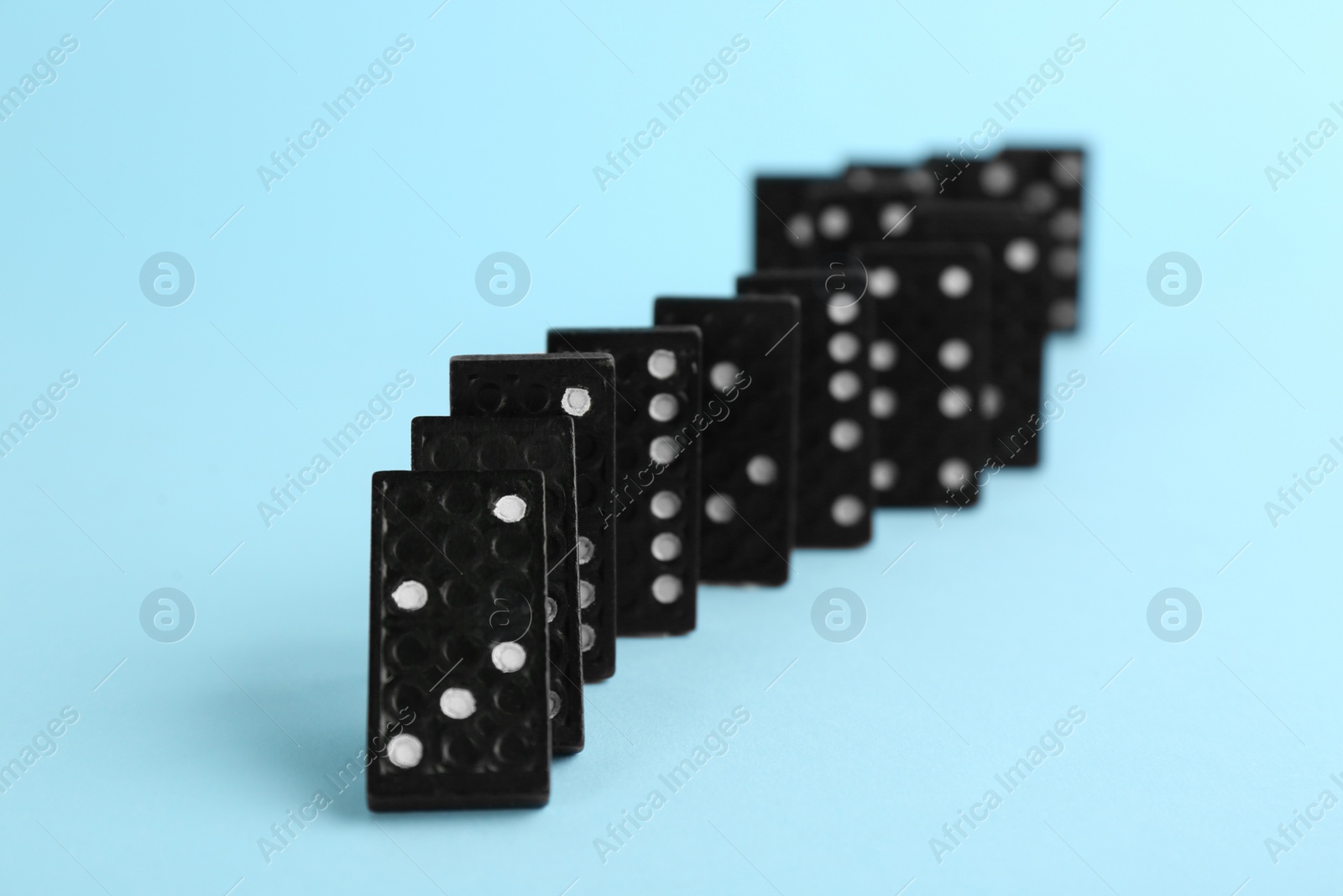 Photo of Black domino tiles falling on light blue background