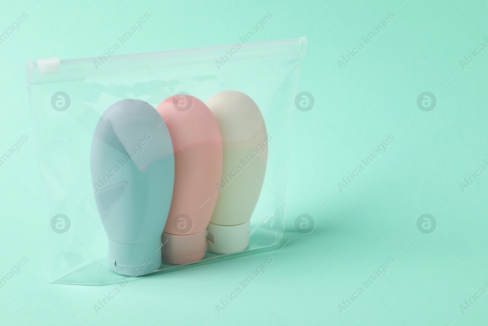 Photo of Cosmetic travel kit in plastic bag on turquoise background. Space for text