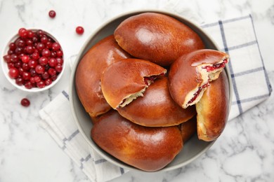 Delicious baked cranberry pirozhki in bowl on white marble table, flat lay