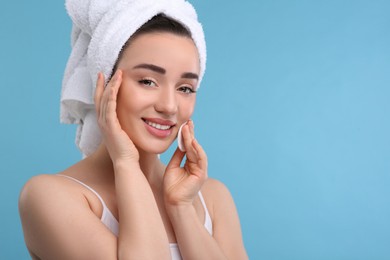 Beautiful woman in terry towel removing makeup with cotton pad on light blue background, space for text