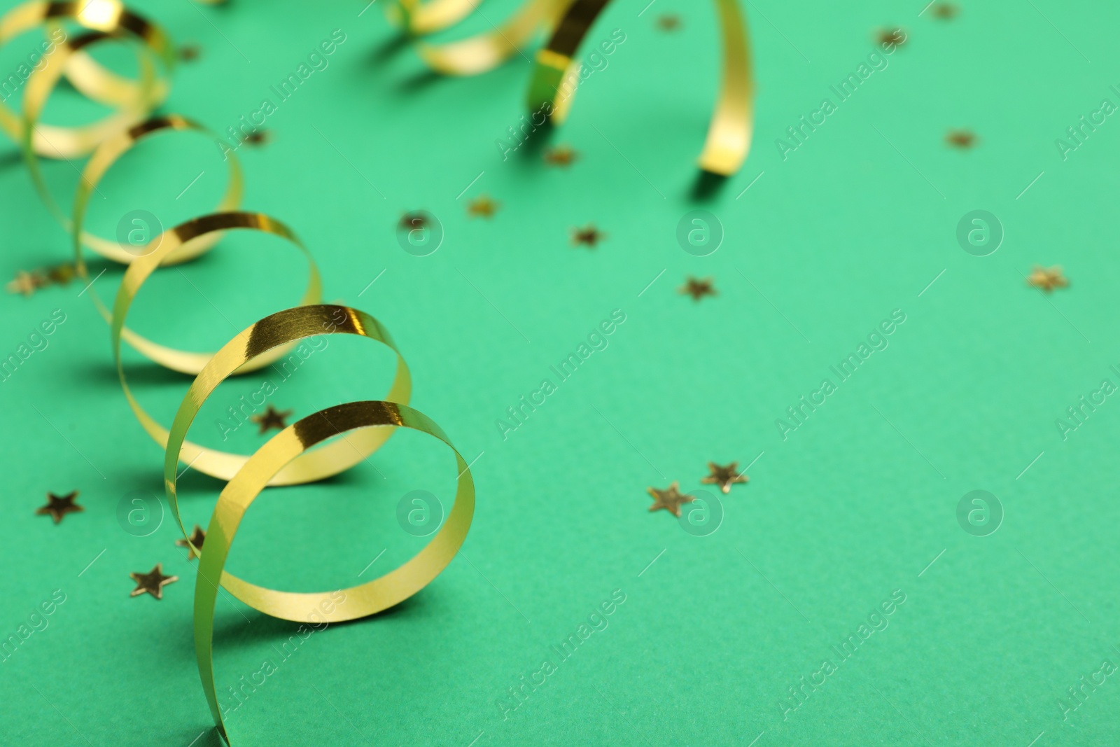Photo of Shiny golden serpentine streamers and confetti on green background, closeup. Space for text