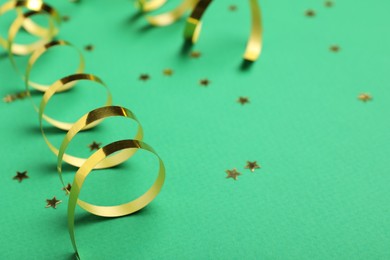Photo of Shiny golden serpentine streamers and confetti on green background, closeup. Space for text