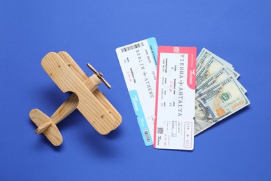 Photo of Dollars, wooden model of plane and tickets on blue table, flat lay. Business trip