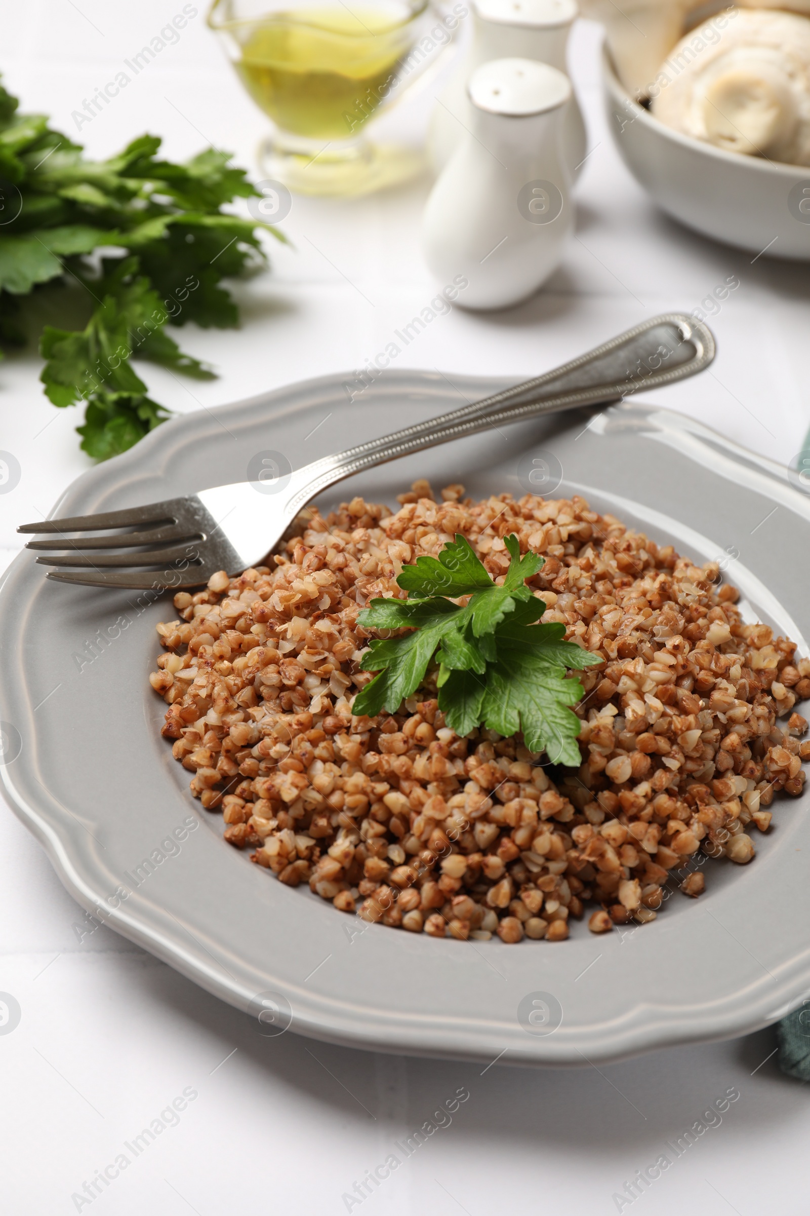 Photo of Tasty buckwheat with fresh parsley and fork on white tiled table