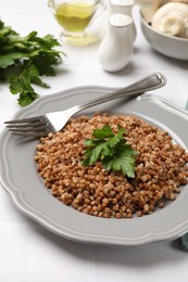 Photo of Tasty buckwheat with fresh parsley and fork on white tiled table