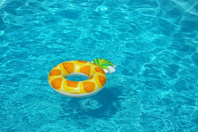Photo of Bright inflatable pineapple ring floating in swimming pool on sunny day. Space for text