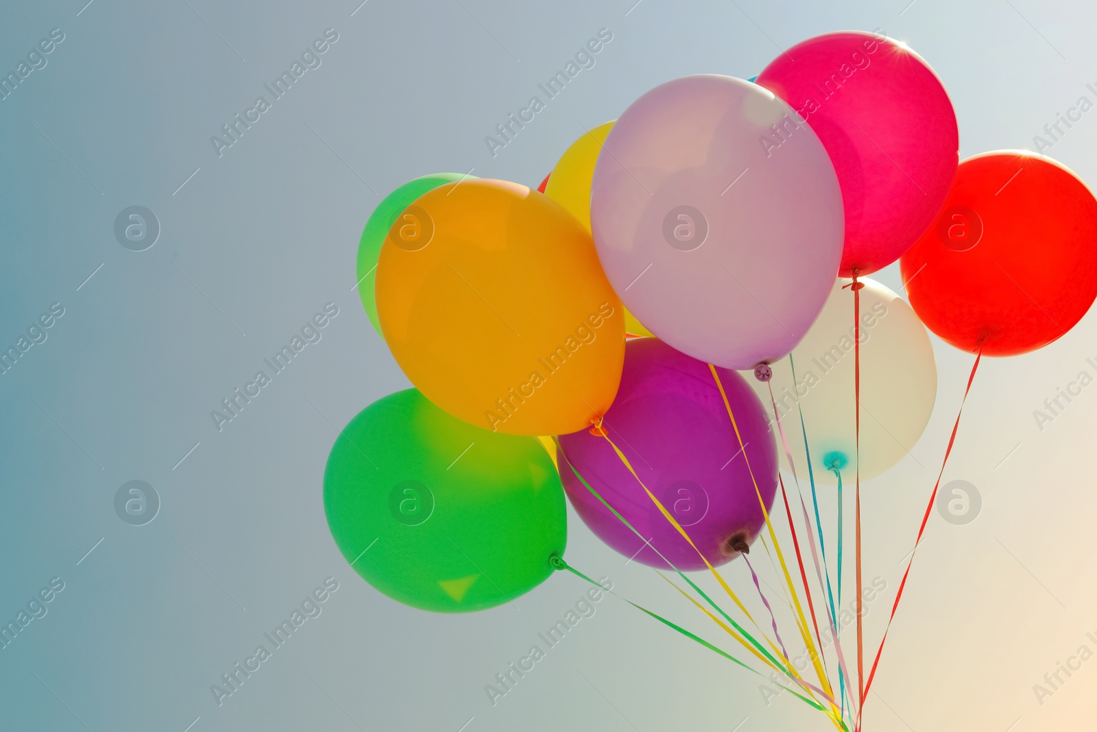 Image of Colorful balloons flying in blue sky on sunny day Space for text