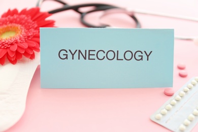 Photo of Card with word GYNECOLOGY, menstrual pad and birth control pills on color background