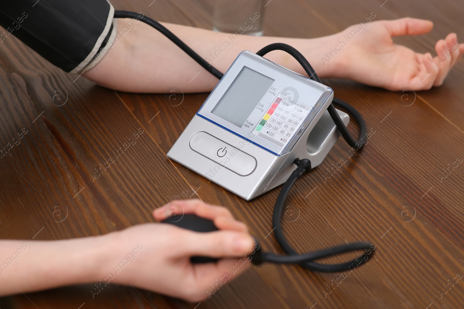 Photo of Woman checking blood pressure at wooden table indoors, closeup