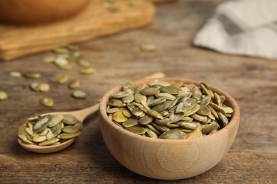 Photo of Bowl and spoon of raw peeled pumpkin seeds on wooden table