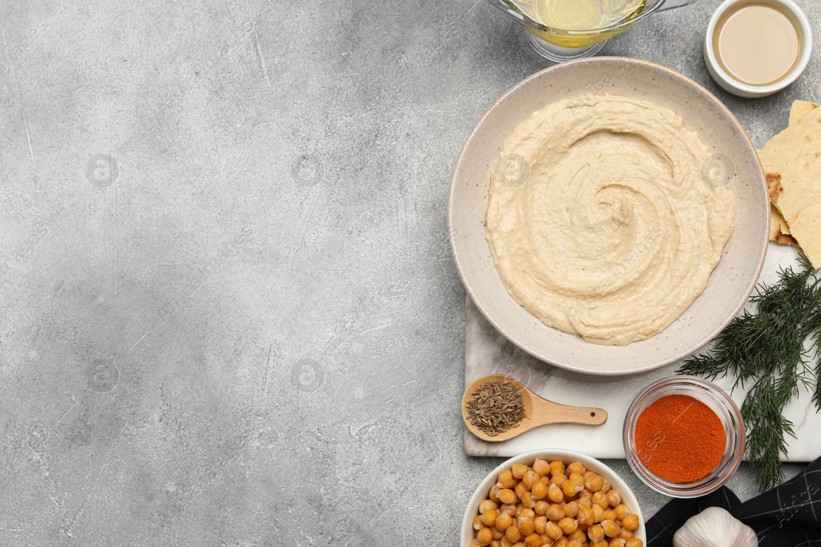 Photo of Bowl with delicious hummus and different ingredients on light grey table, flat lay. Space for text