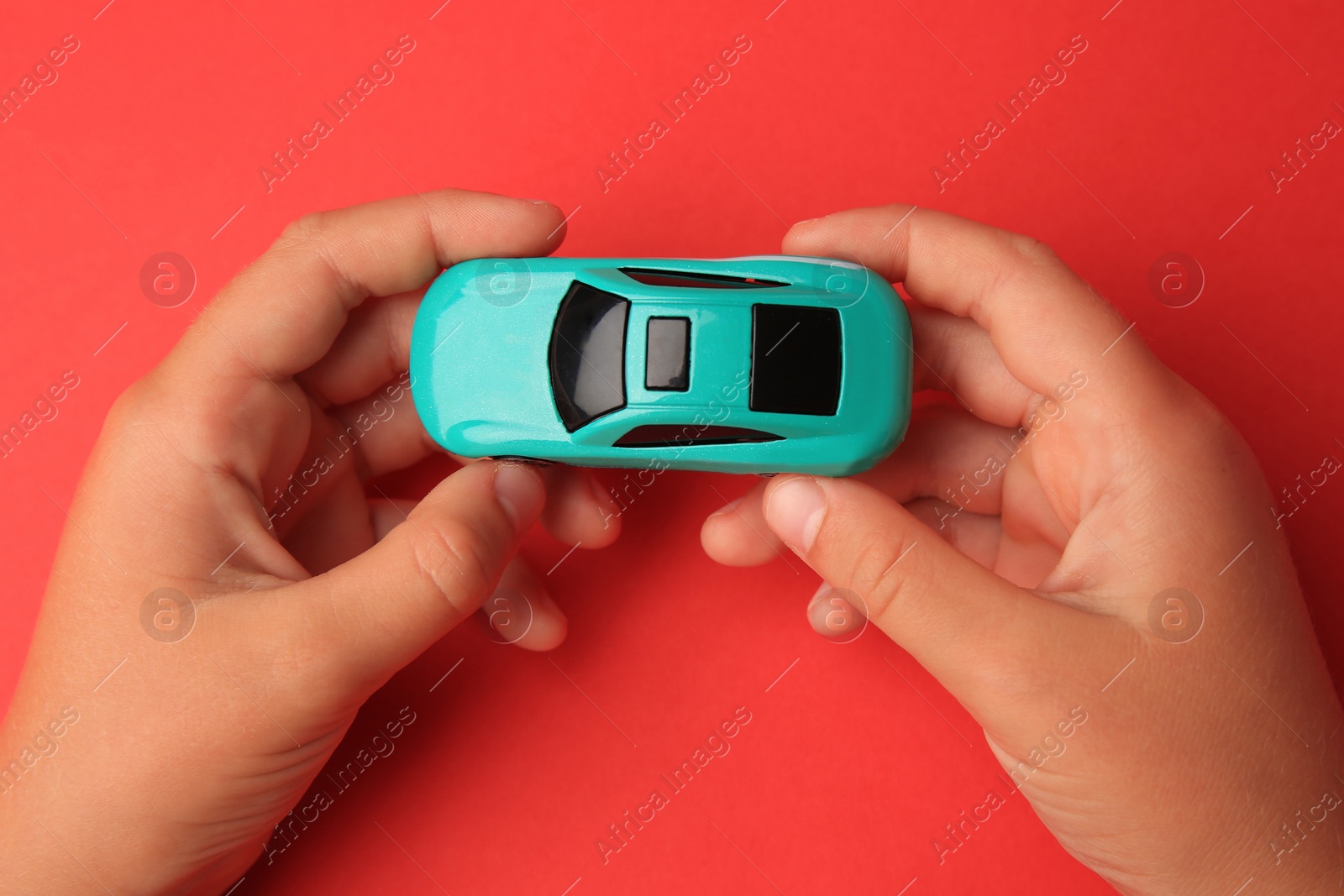 Photo of Child holding toy car on red background, top view