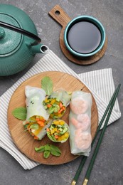 Tasty spring rolls served on grey textured table, flat lay