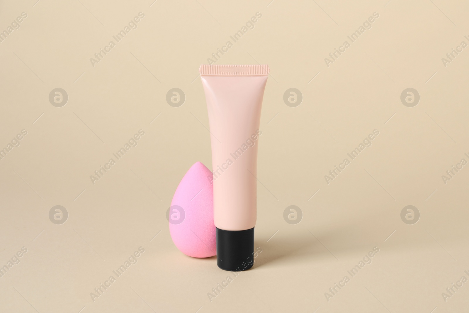 Photo of Tube of skin foundation and sponge on beige background. Makeup product