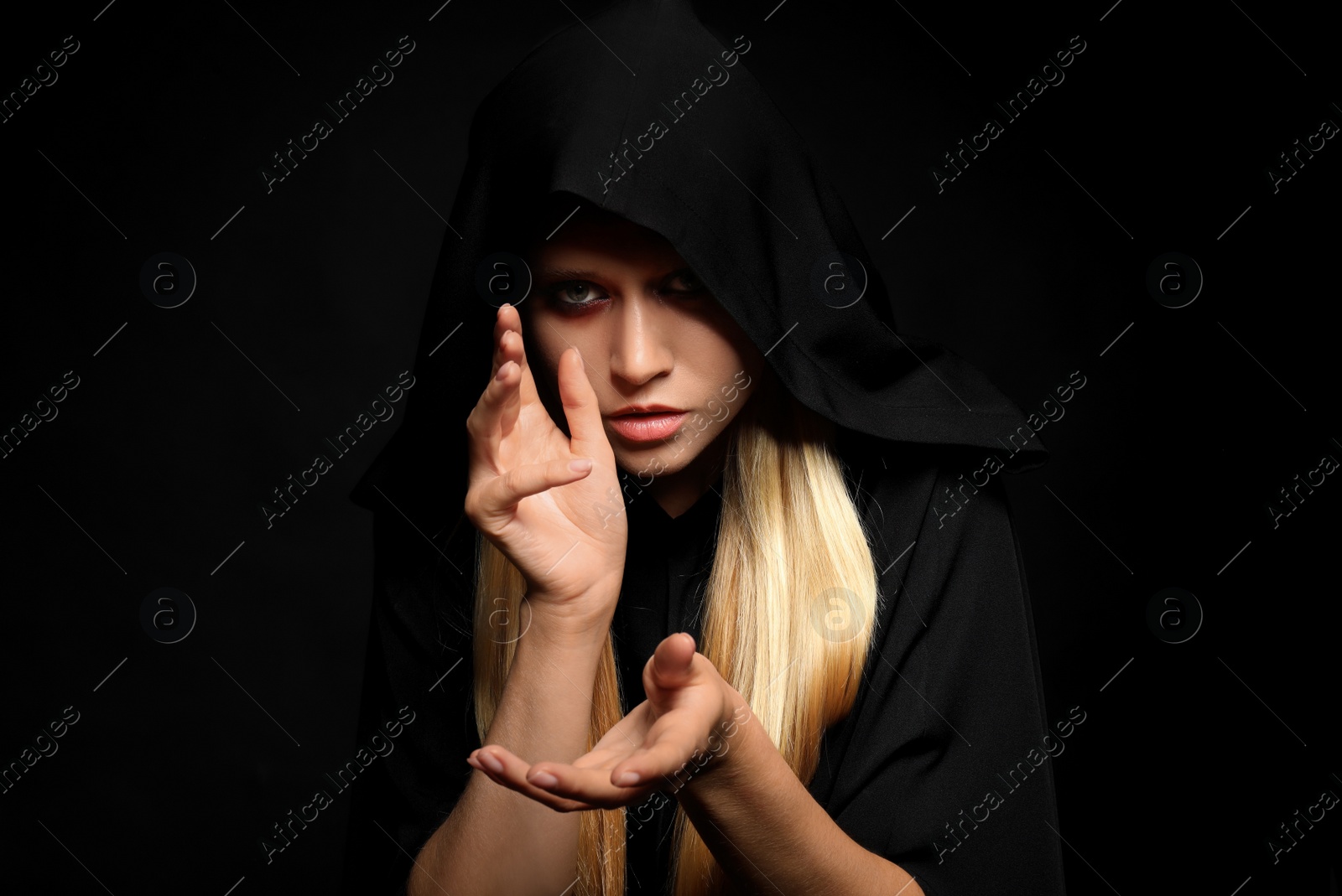 Photo of Witch in black mantle on dark background. Scary fantasy character