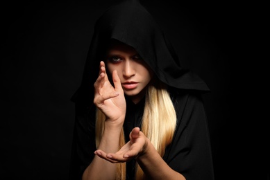 Photo of Witch in black mantle on dark background. Scary fantasy character