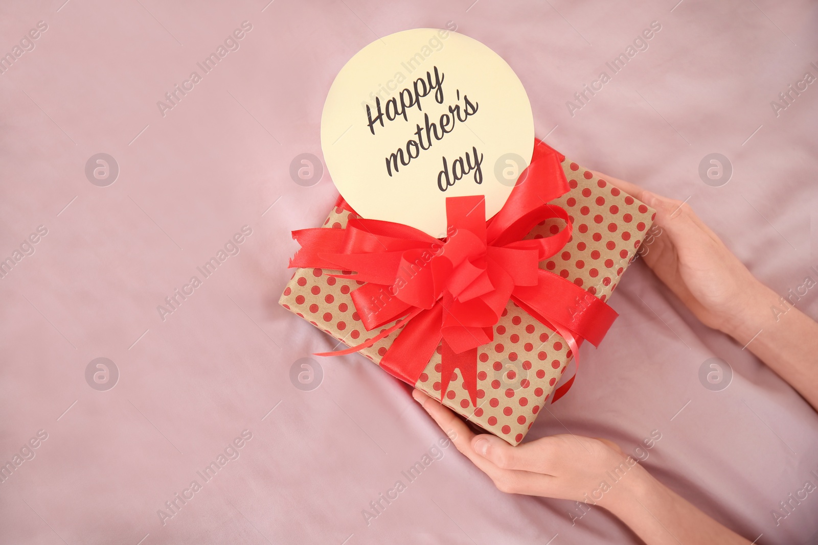 Photo of Little child putting gift box for Mother's Day on bed