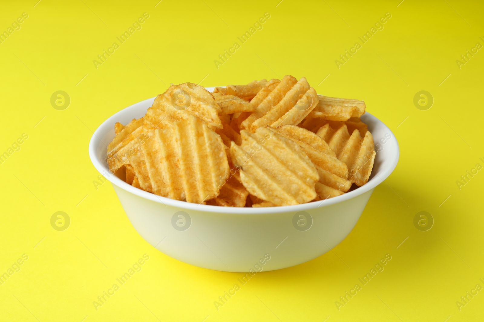 Photo of Bowl of tasty ridged potato chips on yellow background