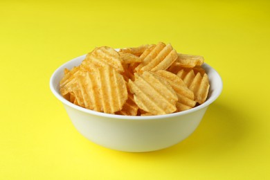 Bowl of tasty ridged potato chips on yellow background