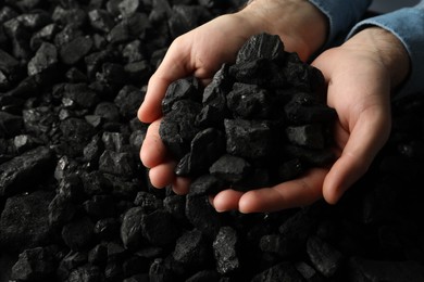 Photo of Man holding coal in hands over pile, closeup. Space for text