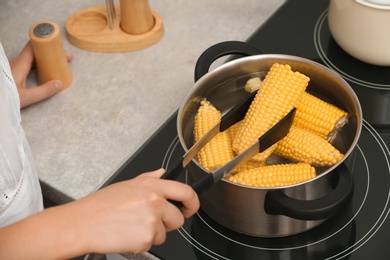 Photo of Woman preparing corn in stewpot on stove, closeup