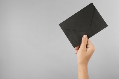 Photo of Woman holding black paper envelope on light grey background, closeup. Space for text