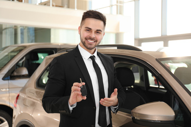 Photo of Young salesman with key near car in dealership