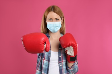 Woman with protective mask and boxing gloves on pink background. Strong immunity concept