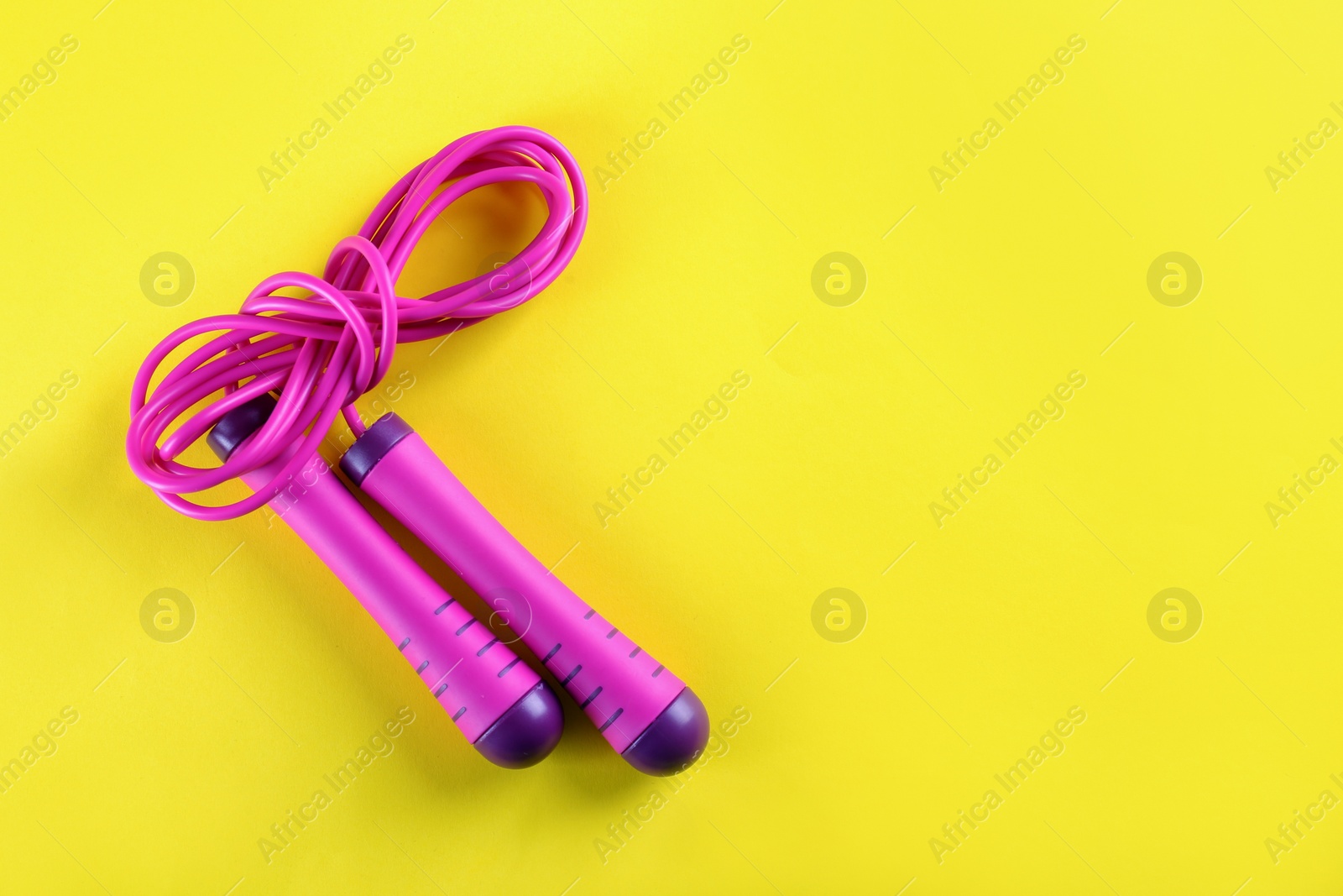 Photo of Skipping rope on yellow background, top view. Space for text