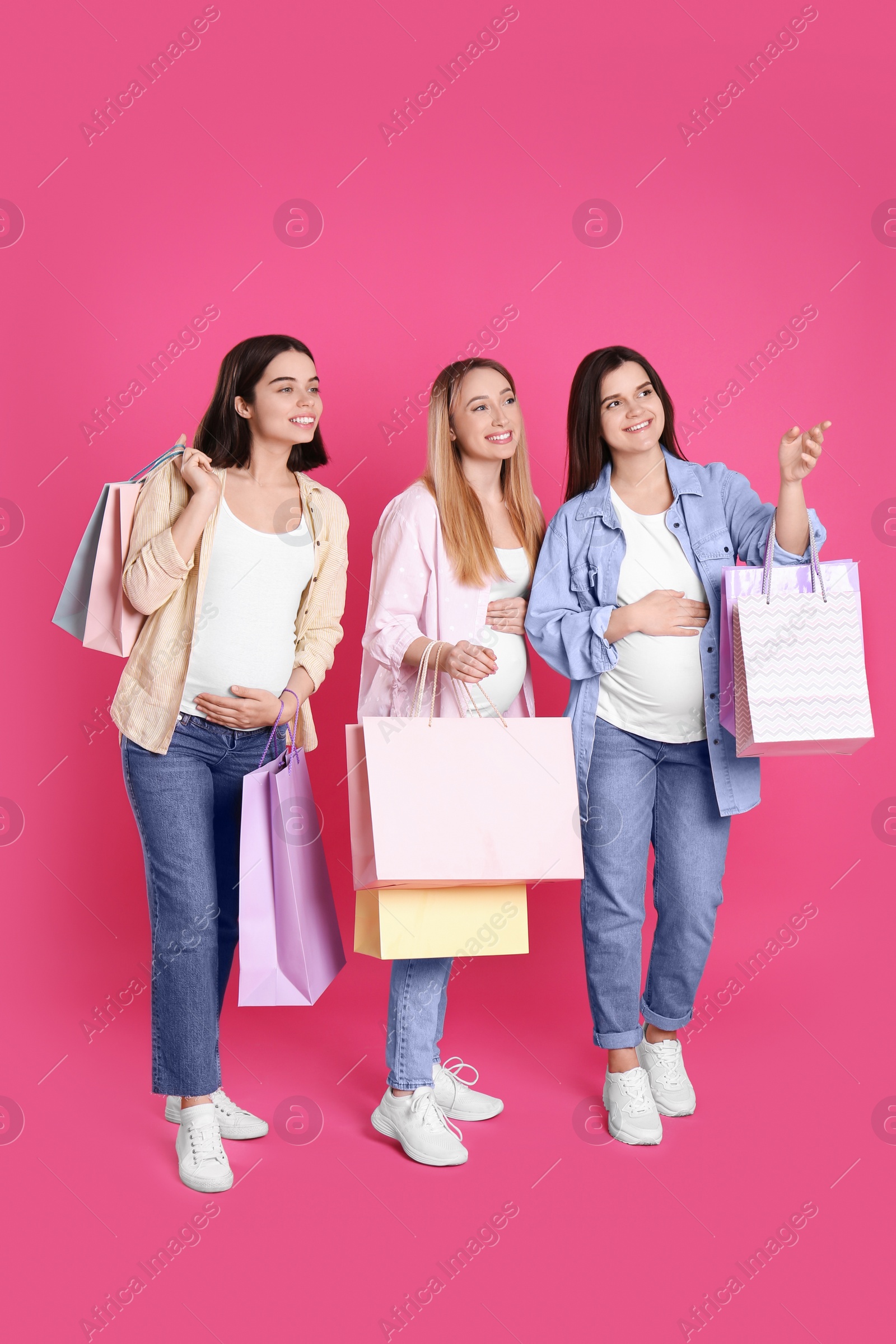 Photo of Happy pregnant women with shopping bags on pink background