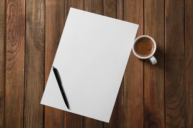 Blank paper sheet, pen and cup of coffee on wooden table, flat lay. Space for text