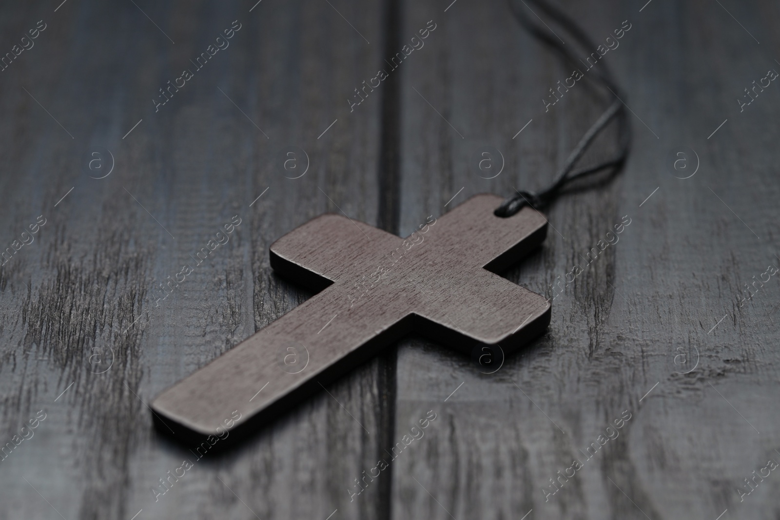 Photo of Christian cross on black wooden table, closeup